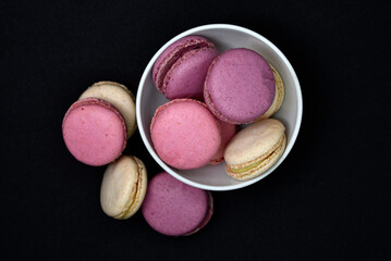 Macaroons in a white plate on a black background. Macaroons in a ceramic bowl. Colorful sweet cookies.