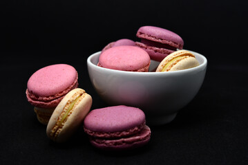 Macaroons in a white plate on a black background. Macaroons in a ceramic bowl. Colorful sweet...