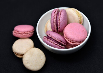 Macaroons in a white plate on a black background. Macaroons in a ceramic bowl. Colorful sweet cookies.