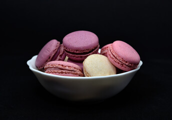 Macaroons in a white plate on a black background. Macaroons in a ceramic bowl. Colorful sweet cookies.