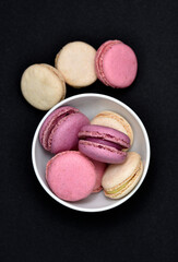 Macaroons in a white plate on a black background. Macaroons in a ceramic bowl. Colorful sweet cookies.