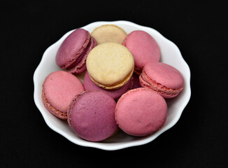 Macaroons in a white plate on a black background. Macaroons in a ceramic bowl. Colorful sweet cookies.
