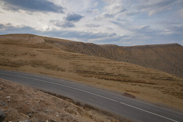 Highway passing through arid mountains on a beautiful cloudy day. Strips on a hillside. Soil erosion, roadside slope.