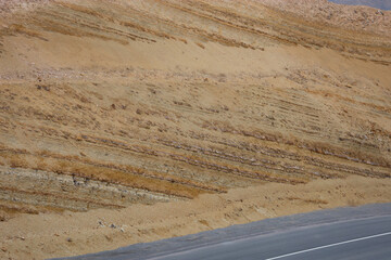 Arid striped land near an asphalt road. Strips on a hillside. Soil erosion, roadside slope.