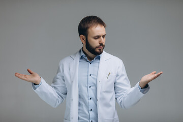 In search of right medical solution. Handsome young doctor in white uniform stretching out his arms while standing against grey background