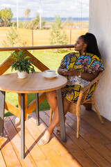 African american woman drinking tea on cozy balcony or terrace wooden country house in weekend on summer morning. Diversity and inclusion and well being concept