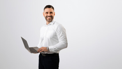 Happy successful middle aged businessman in white shirt working with laptop and looking aside at copy space, panorama