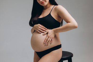 Pregnant woman touching her belly and posing on grey background.