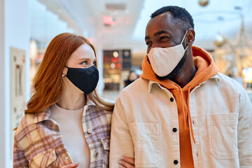 two cheerful smiling lovers in black masks walking, having great time together indoors, holding hands, hugging arm. family, love, relationship