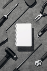 Flat lay composition with set of home repair tools and opened notebook on grey stone background. Top view pattern with copy space.
