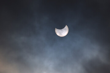 Partial eclipse of the sun on a cloudy sky with visible sunspots on its surface.