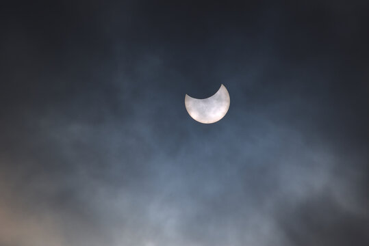 Partial eclipse of the sun on a cloudy sky with visible sunspots on its surface.