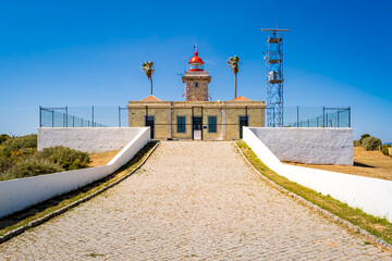 Backside view of the fenced lighthouse Farol da Ponta da Piedade from the driveway, with closed...