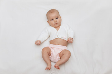 A newborn girl in a white knitted blouse and pink knitted underpants is lying on a white blanket.