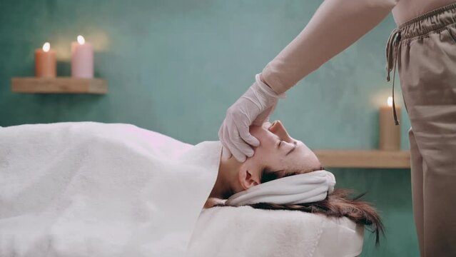 Cosmetologist makes a buccal massage of the patient's facial muscles in spa. Anti-aging massage technique. Side view.