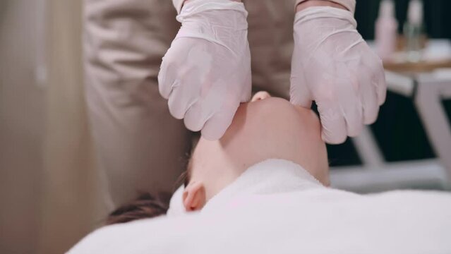 Cosmetologist makes a buccal massage of the patient's facial muscles in spa. Close up of hands.