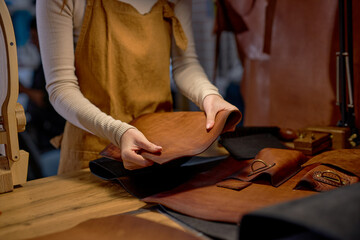 hands touching, holding cut leather, close up cropped side view shot.Working process of sewing leather bag, purse, wallet by hand