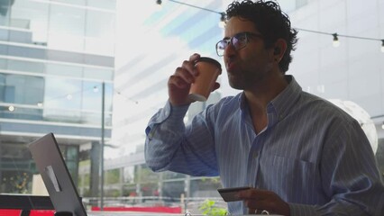 Middle-aged latin man having a coffee before making an online purchase with his credit card. 4k video.