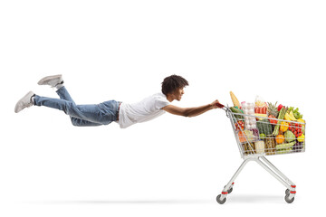 African american guy flying and holding a shopping cart with healthy food