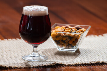 Glass of Belgian abbey red brown beer and glass bowl with party nuts