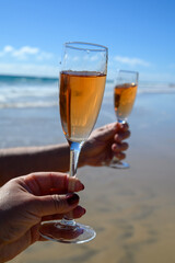 Beach party, hands with glass of rose champagne or cava sparkling wine, view on white sandy tropical beach and blue ocean water, romantic vacation, winter sun on Fuerteventura, Canary, Spain