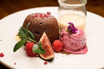 Close-up of chocolate cake with ice and jar of cream served on white plate