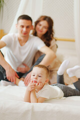 Fototapeta premium funny little son lies in bed against the background of loving mom and dad