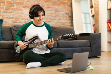 Asian Guy Playing Music On Electric Guitar Near Laptop Indoor