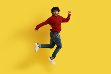 Fototapeta na wymiar Positive eastern guy jumping over yellow studio background