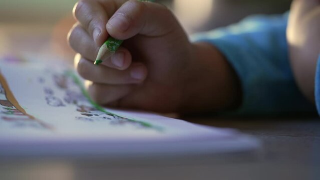 Closeup child hand drawing on paper with green color pencil. Childhood creative development