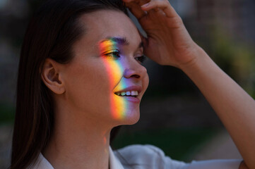 Portrait of caucasian woman with rainbow beam on her face outdoors.