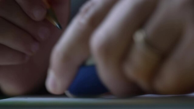 Macro closeup of child hand holding pencil on paper. Erasing content with eraser. Learning mistake concept