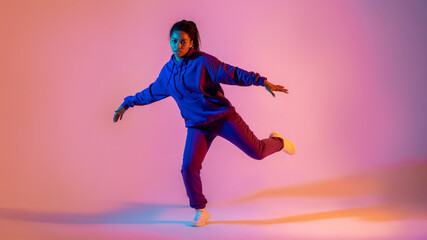 Fototapeta na wymiar Dancing style. Black lady making hip-hop tricks on gradient pink neon background, panorama, full length