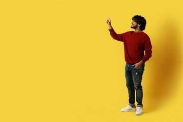 Fototapeta na wymiar Excited indian man touching copy space on yellow