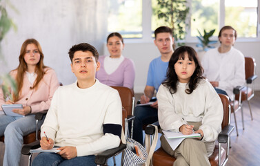 Group of concerned undergraduates listening to lecture and making notes attentively in auditorium