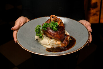 plate with fried pork knuckle garnished with herbs with sauce in female hands