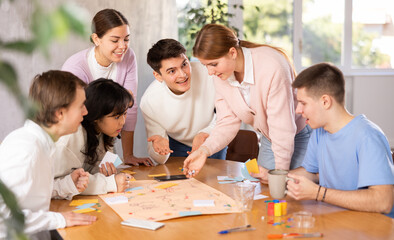 Cheerful adult students playing board game excitedly sitting around the table