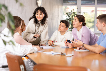 Young teacher discussing her notes with group of grown-up students excitedly around the table - obrazy, fototapety, plakaty