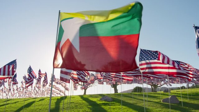 Flag of Myanmar or Burma waving in wind with many American flags on motion background on golden sunset with sun flare. National Myanmar or Burman flag visualizing independence economy partnership