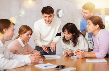 Young teacher discussing his notes with group of grown-up students excitedly around the table