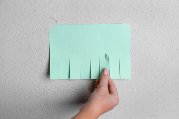 Woman tearing off paper ad from light wall