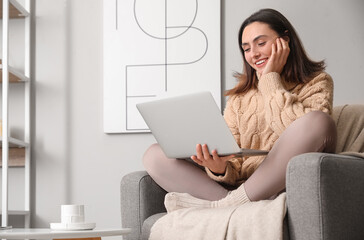 Young woman using laptop in soft armchair at home