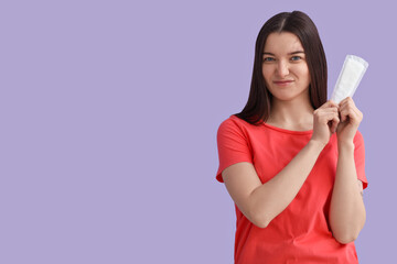 Young woman with menstrual pad on lilac background