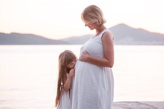 Close-up portrait of little girl hugging pregnant mother. Daughter kisses belly to woman