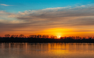 Scenic sunset over the river, the sun sets behind the trees on the horizon. Sunlight reflected in the water