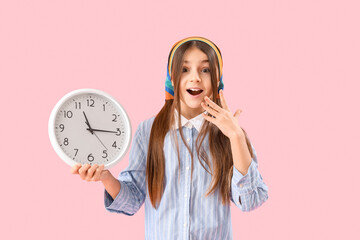 Surprised little girl with wall clock on pink background