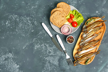 Board with delicious smoked capelin and bread, tomatoes, lettuce, onion on plate against grunge background