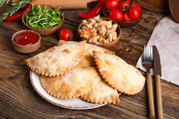 Plate with baked meat empanadas, meat, vegetables, sauce and herbs on wooden background