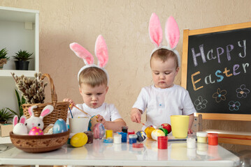 Two children with bunny ears painting Easter eggs at home. Happy Easter concept