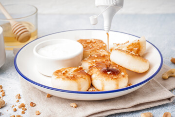 Pouring of caramel syrup onto tasty cottage cheese pancakes on table, closeup